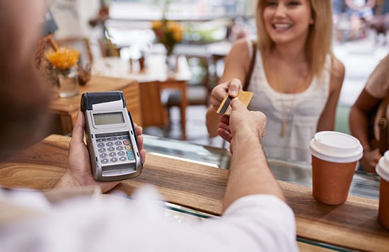 woman making a purchase using her credit card man walking and looking at cell phone
