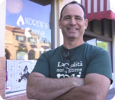 Andrew Steiner, a small business owner, is smiling outside his Andrew’s Cheese Shop.